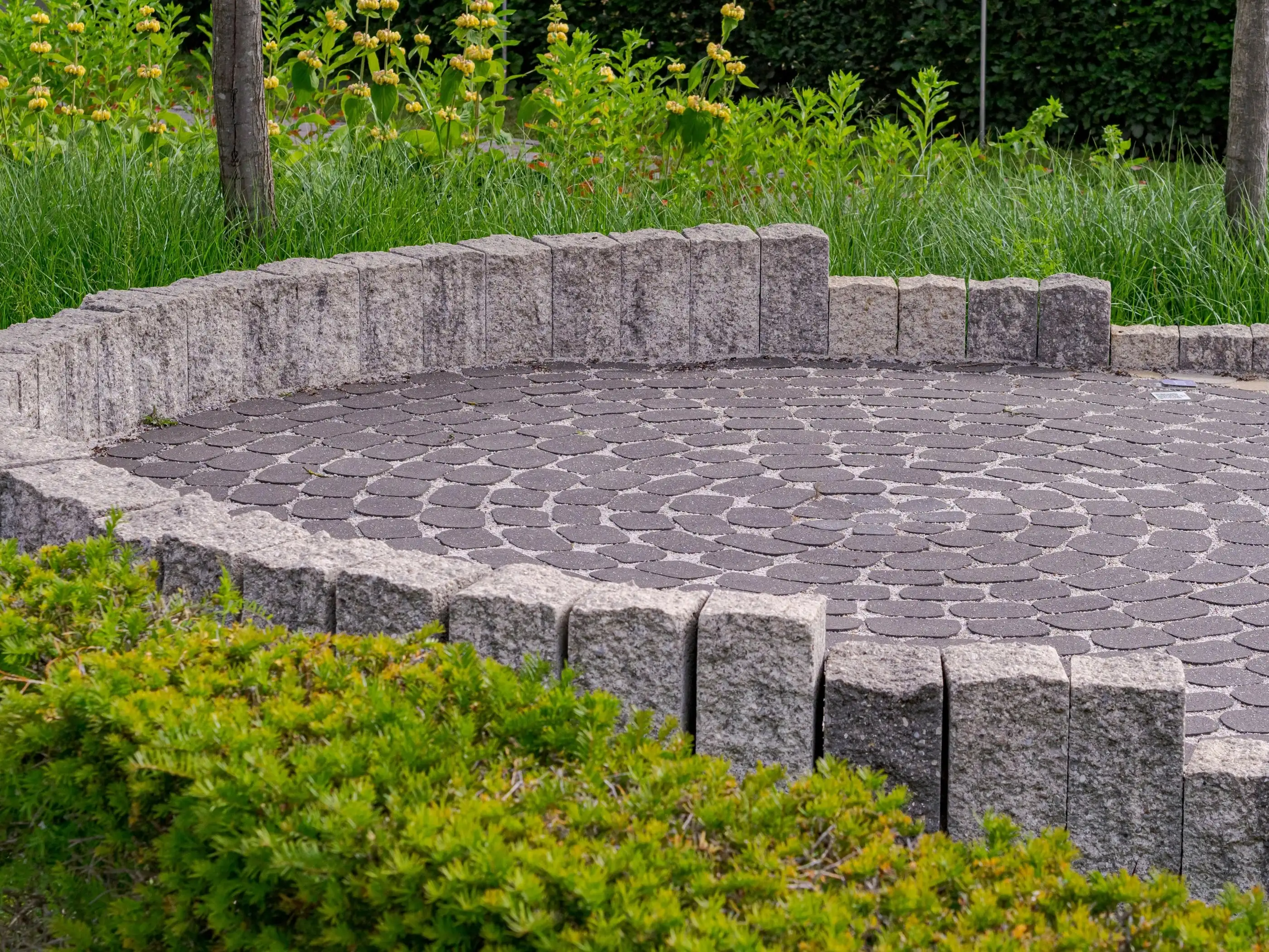 Pavage de granit en cercle bordé de palis de granit.