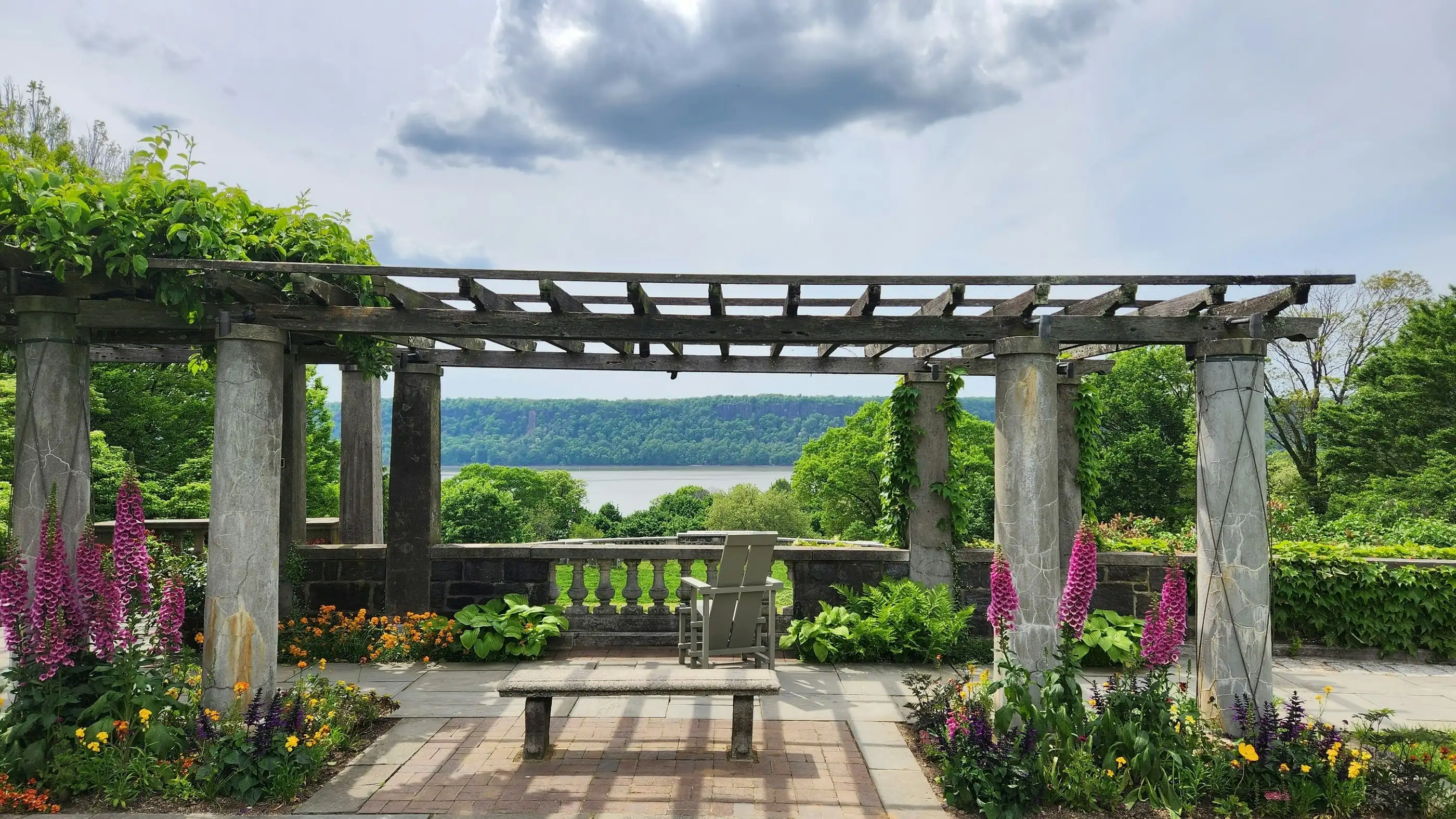 Pergola couverte de plantes grimpantes au-dessus d’une terrasse dallée, avec une vue sur l’eau.