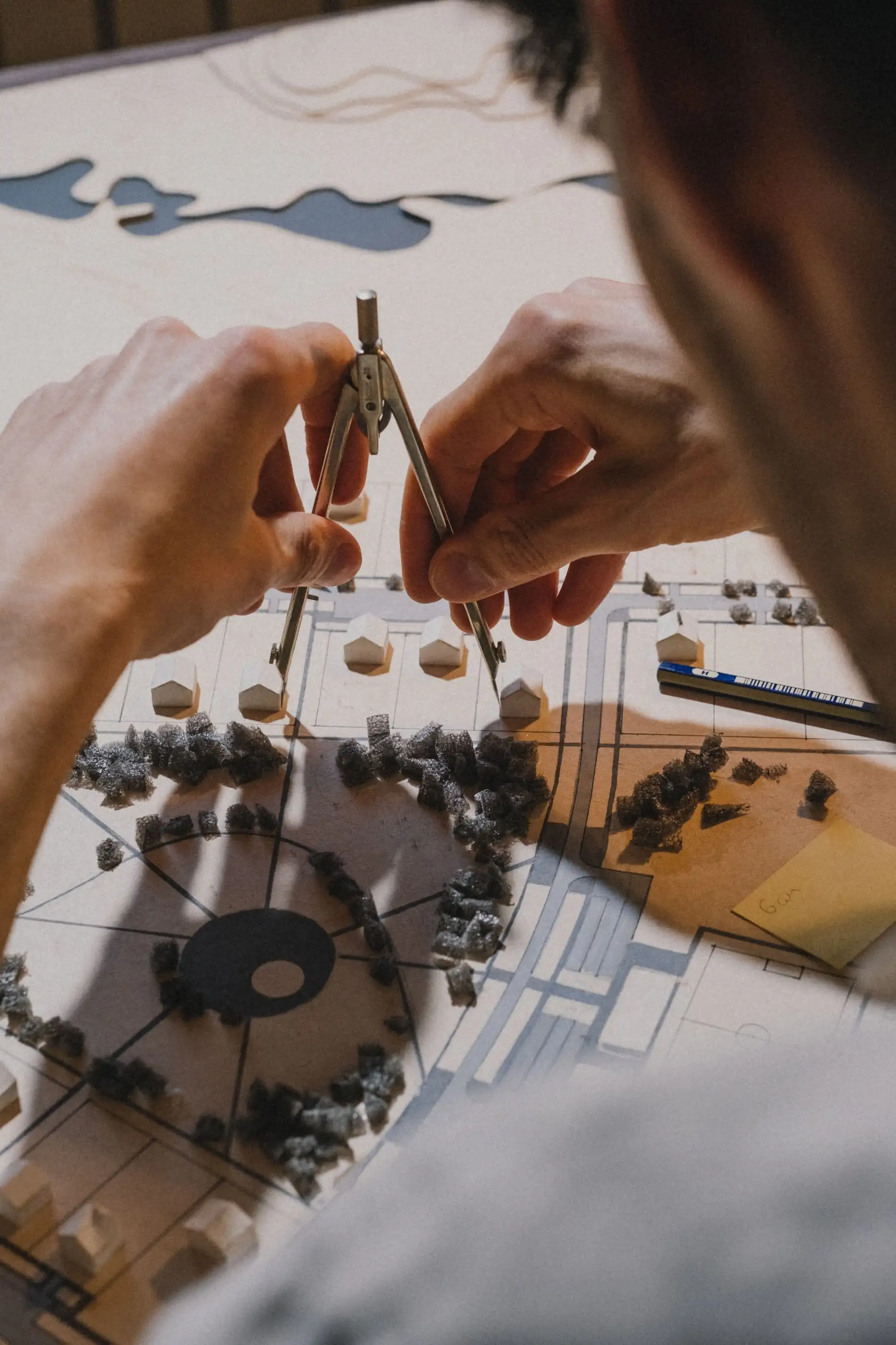 Mains qui prennent une mesure au compas sur un plan de jardin, avec des arbres en maquette.